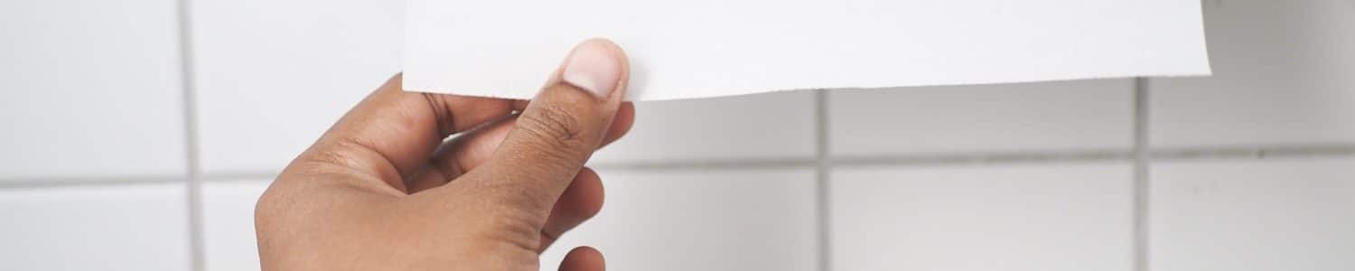 Hand taking paper towel from a dispenser in a clean public restroom with white tiles.