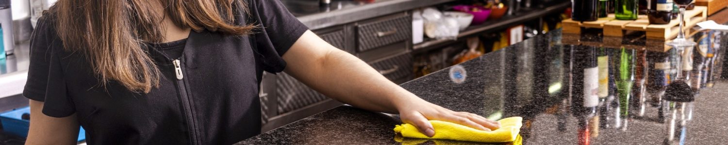 Pretty young waitress in apron bending while using detergent and duster to clean it for new guests of restaurant