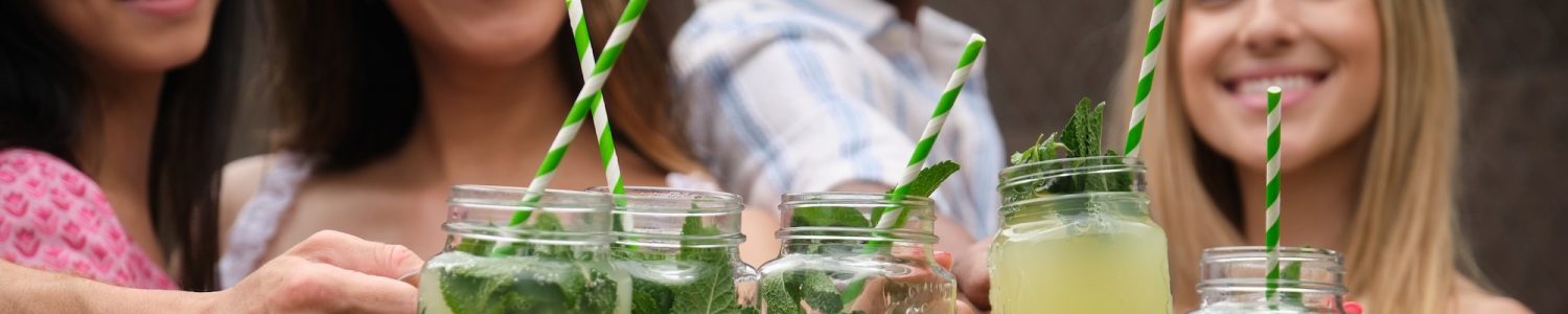 Group of friends holding glass jars with lemonade, mint and green and white striped straws, toasting